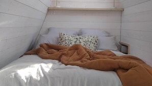 Ein Schlafzimmer mit schrägverdeckter Decke, einem Bett mit weißer Bettwäsche und einer braunen Decke, zwei Nachttischlampen und einem Dachfenster.
