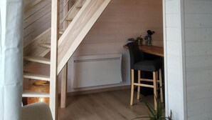 Eine Holztreppe führt zu einer erhöhten Ebene, einem Essbereich mit Tisch und Stühlen sowie einer hängenden Leuchte.