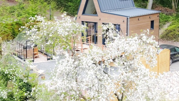 Ein modernes Haus mit geneigtem Dach, großen Fenstern und einem Wintergarten aus Glas.