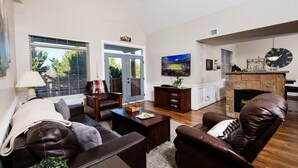Una sala de estar con chimenea, televisor y un ventanal con persianas.