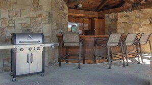 Un área de cocina al aire libre con una parrilla empotrada, taburetes de bar y un refrigerador.