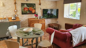 A cozy living room with a dining table, chairs, a red sofa, a television, and a painting on the wall.