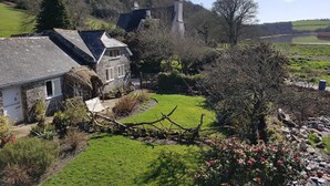A stone house with a thatched roof, surrounded by a well-maintained garden and a view of a lake.