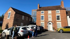 Un hôtel à la façade en briques, une enseigne indiquant « The Crown Inn », et plusieurs voitures garées.