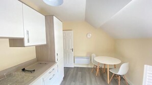 Une cuisine de taille réduite avec des meubles blancs, un plan de travail en bois et une table de salle à manger ronde, accompagnée de chaises.