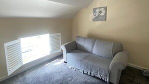 Une pièce avec un canapé gris, une fenêtre avec des volets blancs et un tableau accroché au mur.