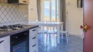 Una cocina moderna con una isla central, un comedor con mesa y sillas, y vistas a través de un ventanal.
