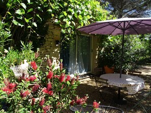 Een tuin met een stenen muur, een tafel met een paarse parasol en bloeiende rode planten.