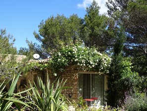 A stone building with a small patio and a red chair. - Chambre d hôte (Murs)