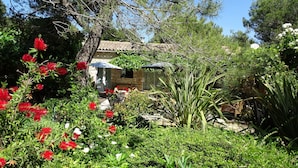 A stone house with a tiled roof, surrounded by lush greenery and red flowering plants. - Chambre d hôte (Murs)
