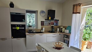 A compact kitchen with a dining area, a built-in oven, a sink, and a window with a view of greenery. - Chambre d hôte (Murs)