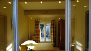 A bedroom with a bed, a potted plant, a window, and a door. - Chambre d hôte (Murs)