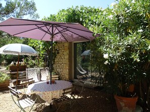 A patio with a round table and chairs, a purple umbrella, and a stone wall. - Chambre d hôte (Murs)