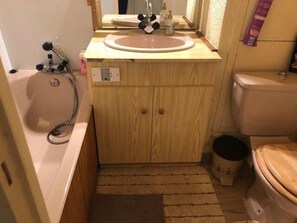 Ein kleines Badezimmer mit einem Holzlagerfläschchen, einem Waschbecken, einer Toilette und einer Dusche.