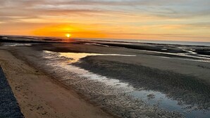 Une plage au coucher du soleil, avec du sable mouillé et un ciel dégagé.