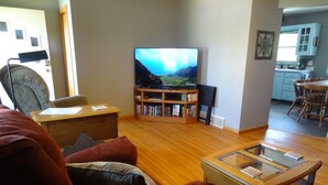 Una sala de estar con televisor, estanterías, un sofá y una mesa de centro de vidrio.