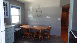 Un área de comedor con una mesa y sillas de madera, una ventana y una pared decorada con los mensajes 'Thankful' y 'Gather'.