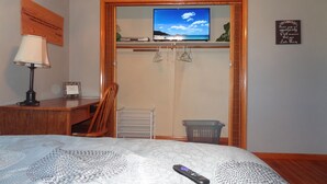 Un dormitorio con cama, televisor sobre un mueble, puerta de madera, escritorio con lámpara y pared con citas motivacionales.