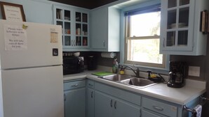Una cocina con gabinetes azul claro, un refrigerador, un microondas, una cafetera y una ventana.