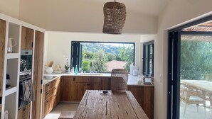 A modern kitchen with wooden cabinetry, a central island, and a large window offering a view of greenery. - "La Chamade" – 180° ocean view – 6 bedrooms – heated pool – near St. Tropez (LA CROIX VALMER)