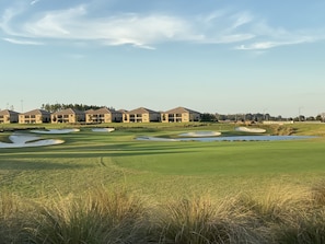 Un campo de golf con búnkeres, un obstáculo acuático y una fila de edificios al fondo.