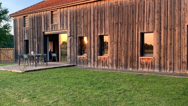 A rustic wooden barn-style building with a red-tiled roof, large windows, and a patio area with outdoor seating. - Tobacco drying shed renovated into a loft, at CAPDROT in Périgord Pourpre (CAPDROT)