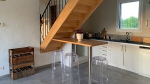 A modern kitchen with a wooden staircase, clear stools, and a window with a view. - Tobacco drying shed renovated into a loft, at CAPDROT in Périgord Pourpre (CAPDROT)
