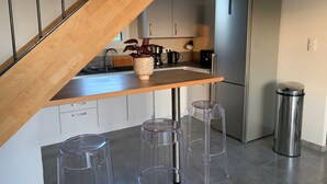 A modern kitchen with a wooden staircase, stainless steel appliances, and clear plastic stools. - Tobacco drying shed renovated into a loft, at CAPDROT in Périgord Pourpre (CAPDROT)