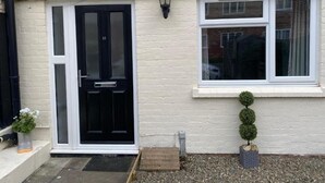 A house with a black front door, a white window, and a small potted plant on the right.