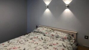 A bedroom with a bed, floral bedding, and two wall-mounted lights.