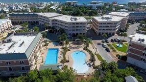 A resort with multiple buildings, a central swimming pool, and a view of the ocean.