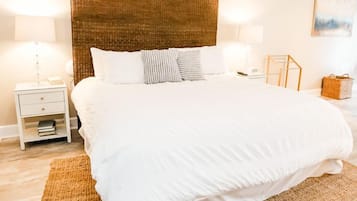 Una cama bien hecha con ropa blanca, un cabecero tejido y una alfombra con textura en el suelo.