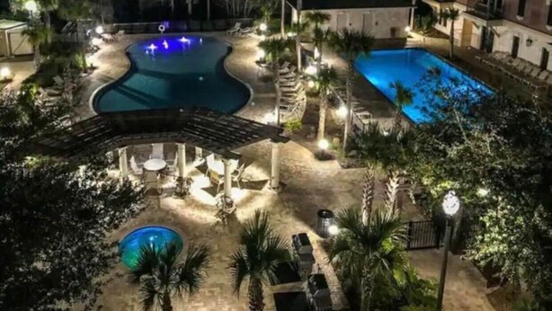 A nighttime view of a resort with multiple swimming pools, a covered seating area, and well-lit pathways.