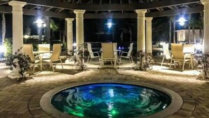 A pool area with a circular pool, white lounge chairs, and a pergola with columns.