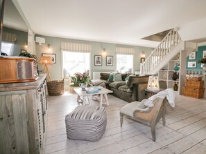 A cozy living room with a wooden coffee table, a striped ottoman, a green sofa, and a staircase leading to an upper level. - Louvain (Helston)