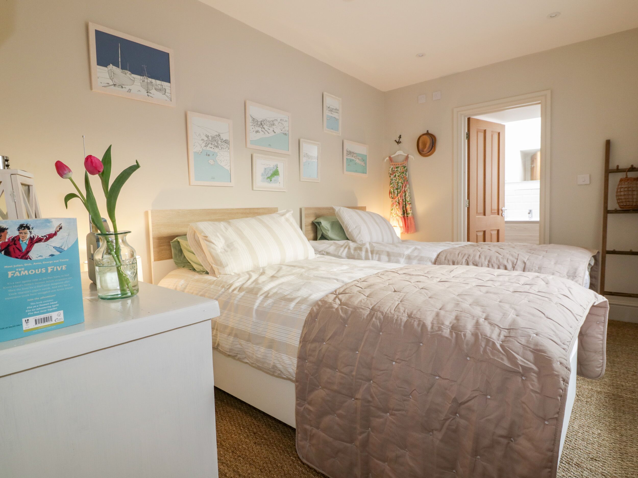 A bedroom with two beds, a desk with a book and a vase of flowers, and wall art.