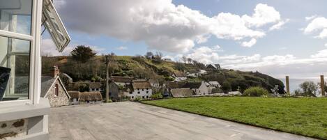 A courtyard with a stone floor, a glass door, and a view of traditional houses on a hillside.