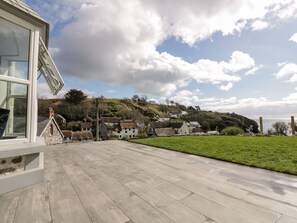 A courtyard with a stone floor, a glass door, and a view of traditional houses on a hillside. - Louvain (Helston)