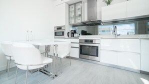A modern kitchen with white cabinetry, stainless steel appliances, and a dining area with white chairs.