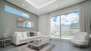 A modern living room with a white sofa, a glass coffee table, and a large window with a view of the city.
