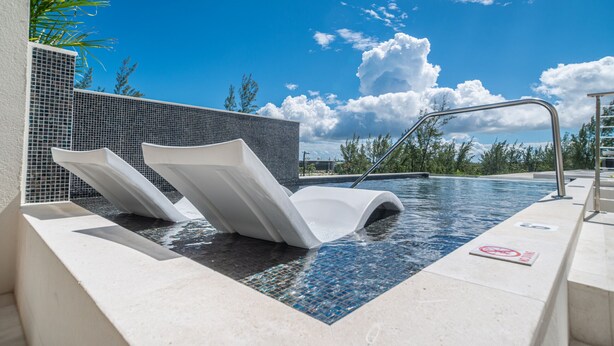 A modern pool area with two white lounge chairs, a clear blue sky, and a no swimming sign.