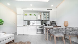 Een moderne keuken met witte kasten, roestvrijstalen apparatuur en een eethoek met rieten stoelen.