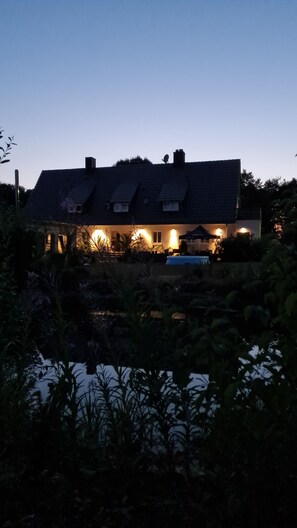 A house with a sloped roof, a swimming pool, and a well-lit exterior.