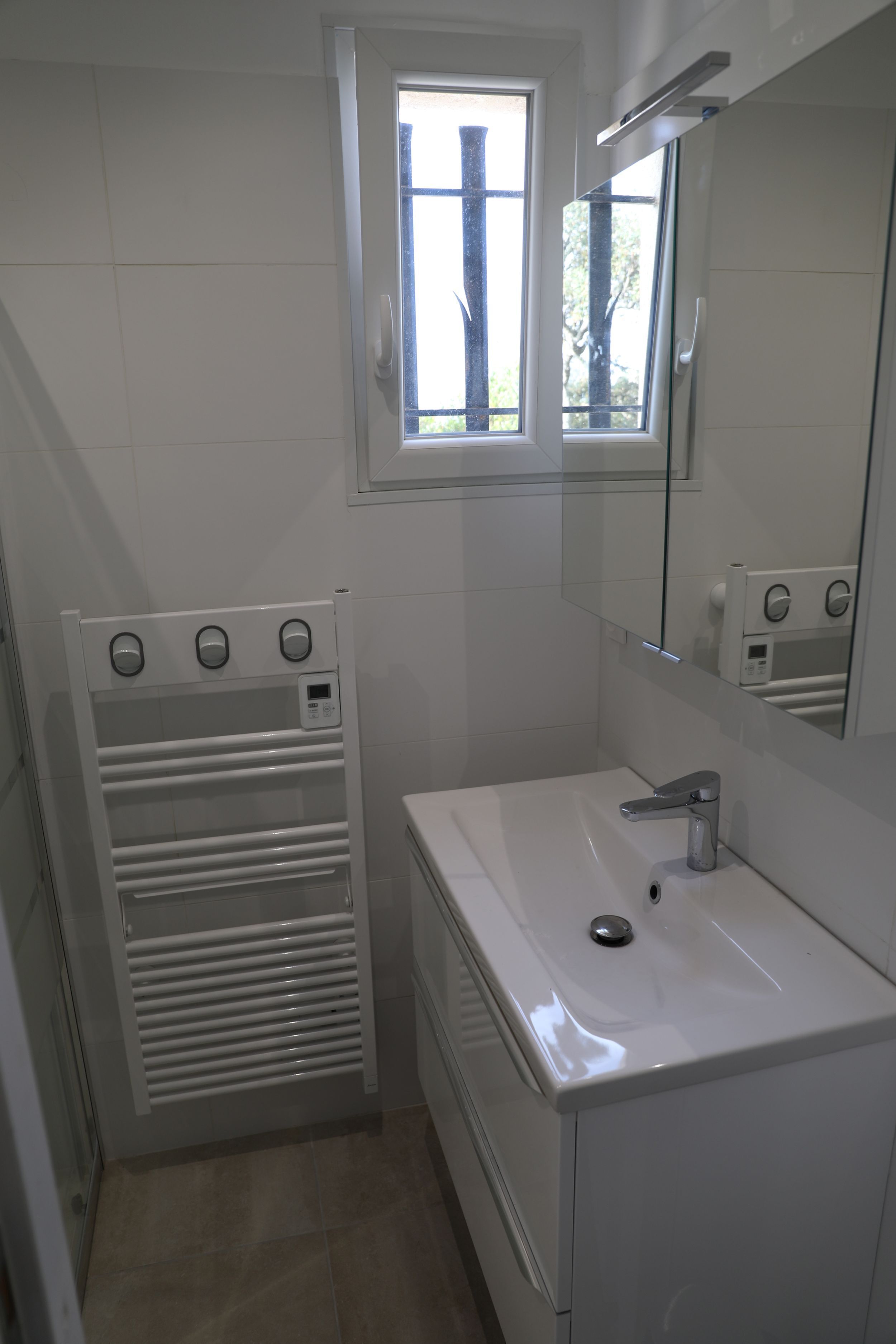 A bathroom with a white sink, a mirror, a towel rack, and a window.