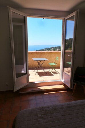Ein Zimmer mit einem Bett und einer Glasschiebetür, die zu einem Balkon mit Tisch und Stühlen im Freien führt.