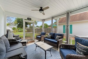 Eine überdachte Terrasse mit Korbmöbeln, einem Deckenventilator und Blick auf den Garten.