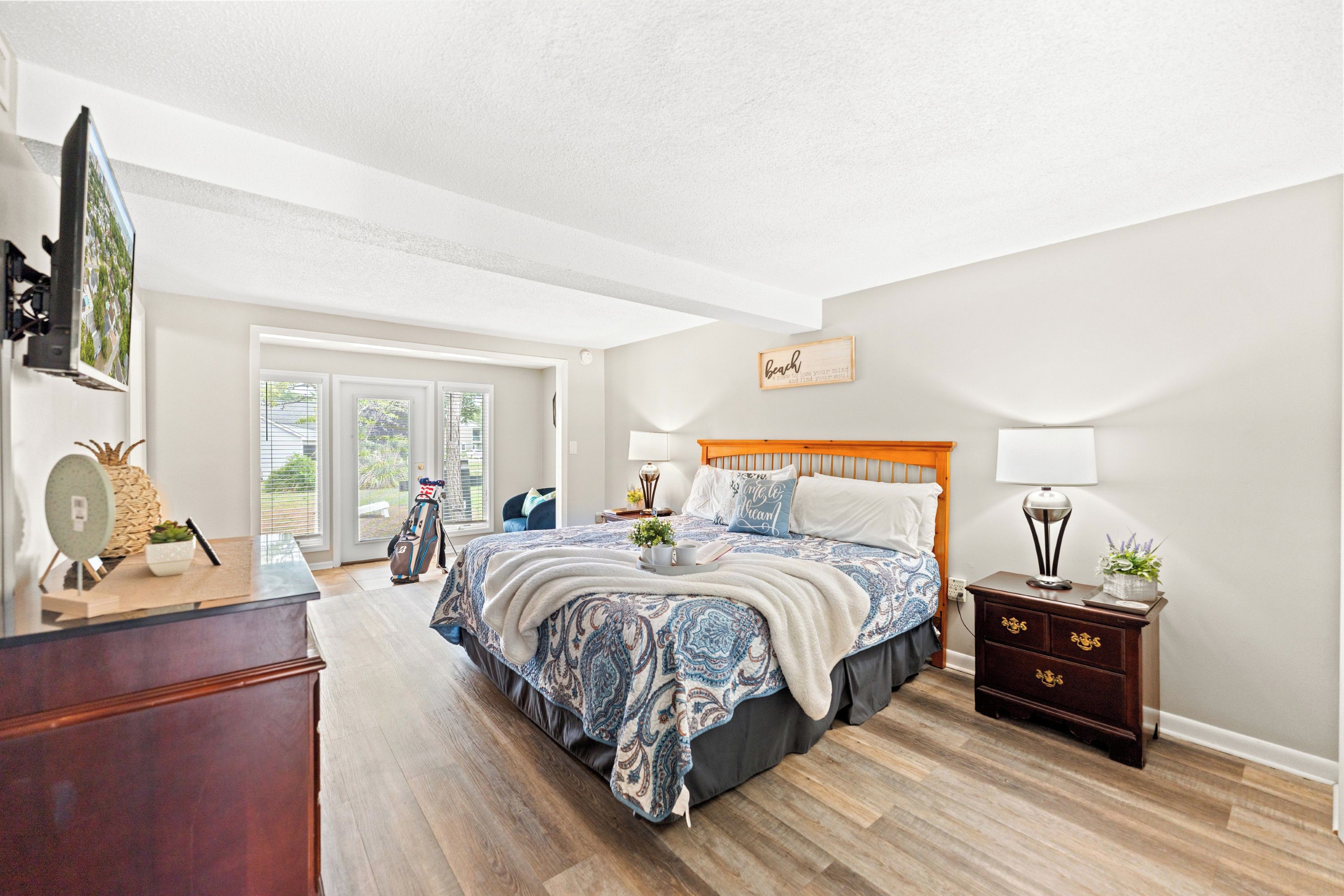A bedroom with a bed, a nightstand, a dresser, and a large window.