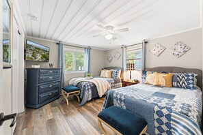 Ein Schlafzimmer mit einem Bett, zwei Nachttischen, einer Kommode, einem Fenster mit Vorhängen und einem Deckenventilator.