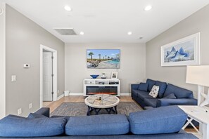 A modern living room with a blue sofa set, a fireplace, a TV mounted on the wall, and a framed picture of a whale.