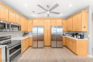 A modern kitchen with wooden cabinets, stainless steel appliances, and a ceiling fan. - 4202 Destination Sand Dollar - Oceanfront Pool (North Myrtle Beach)